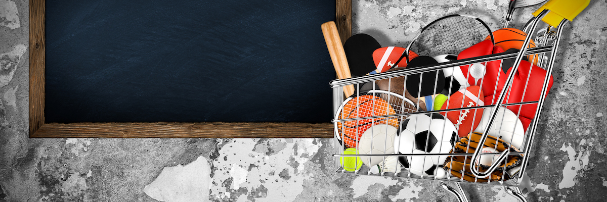 shopping cart filled with sports equipment in front of stone wall with blackboard